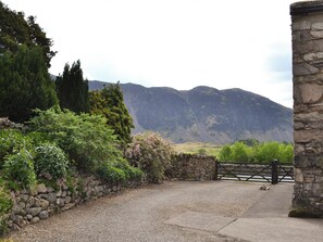 A stone wall, a gravel path, and a gate leading to a mountainous landscape.