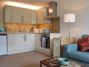A compact kitchen with a microwave, toaster, and oven, a small dining table with a bowl, and a blue sofa with a red pillow. - 2 bedroom accommodation in Wasdale Head, near Gosforth (Wasdale Head, near Gosforth)