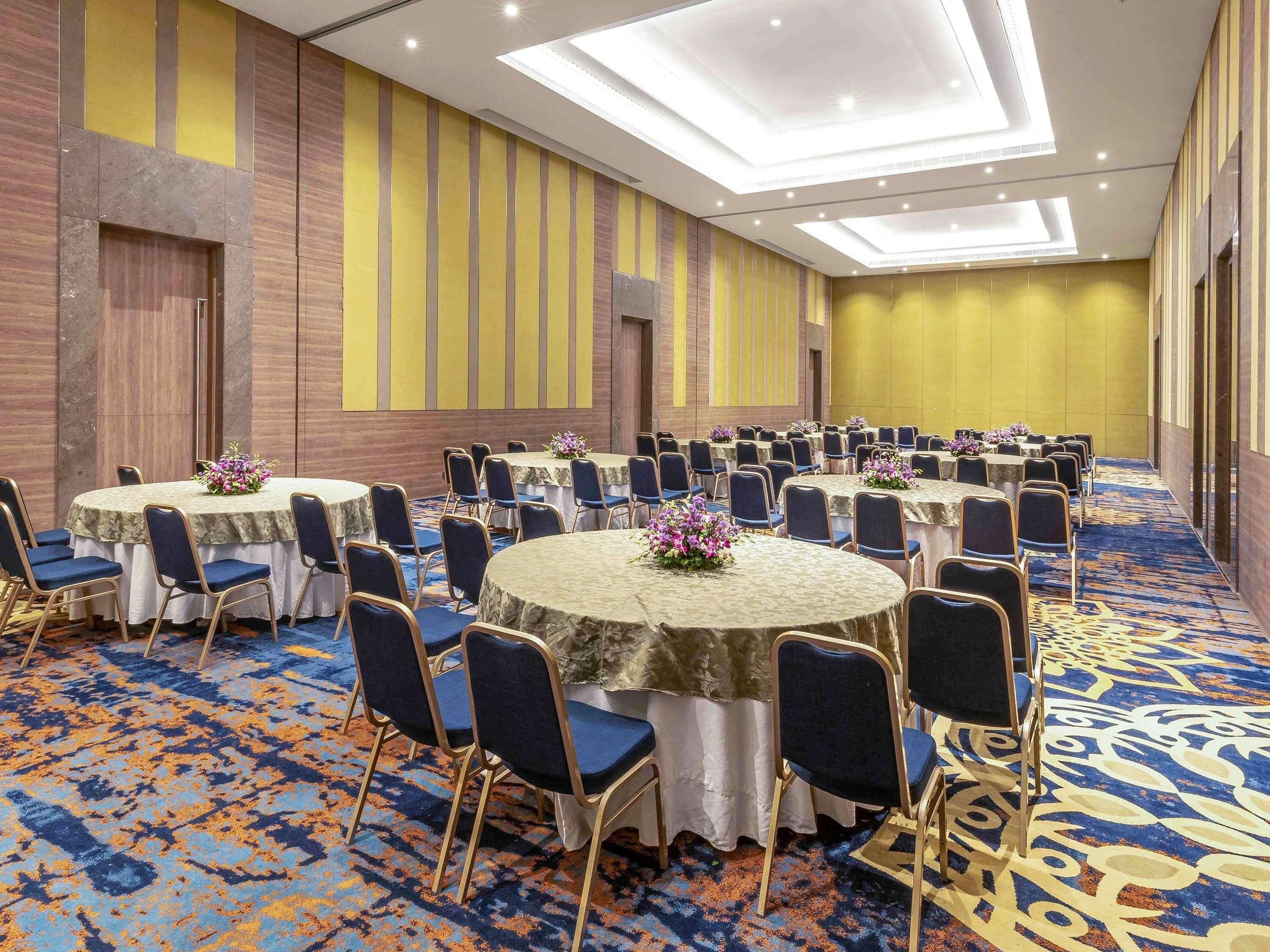 Une salle de conférence dotée de plusieurs tables rondes, de chaises bleues et d’un tapis à motifs.