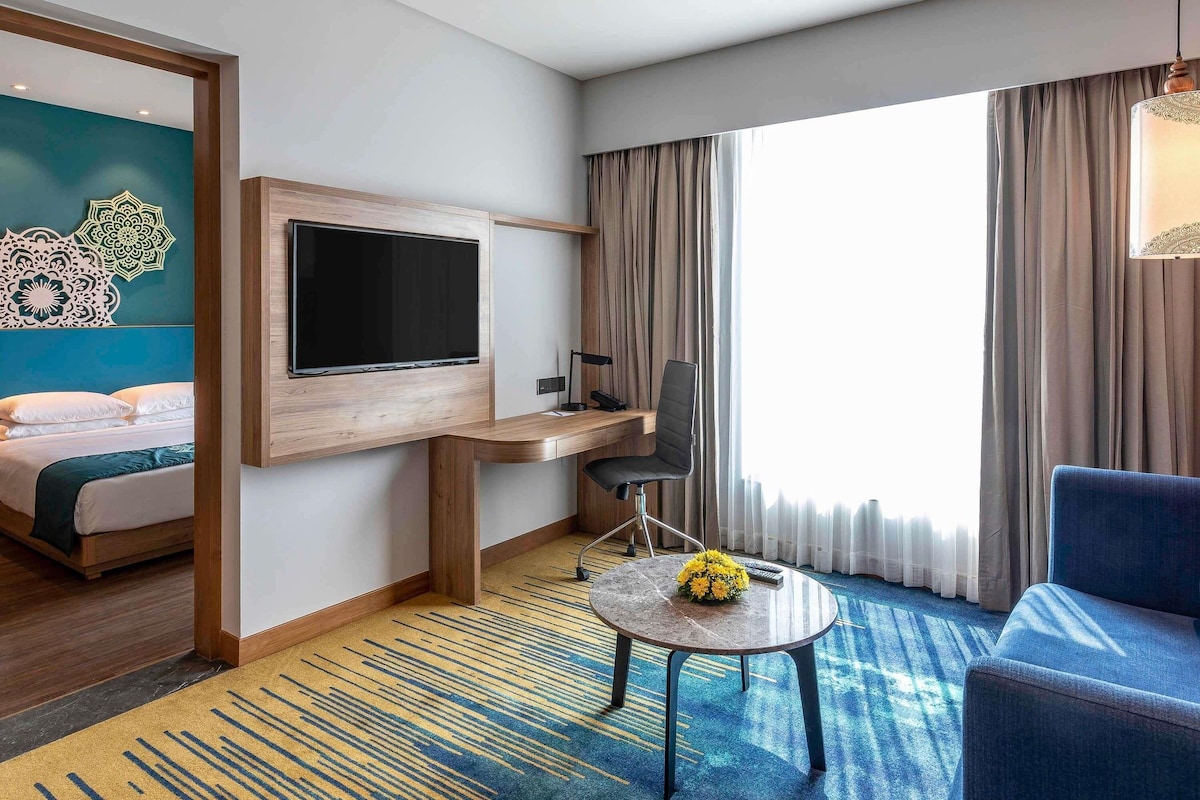 Habitación de hotel con cama, escritorio, televisor, silla y vistas al exterior.