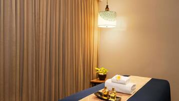 A hotel room with a bed, a bedside table with a lamp, a tray with bottles, and a towel on the bed.