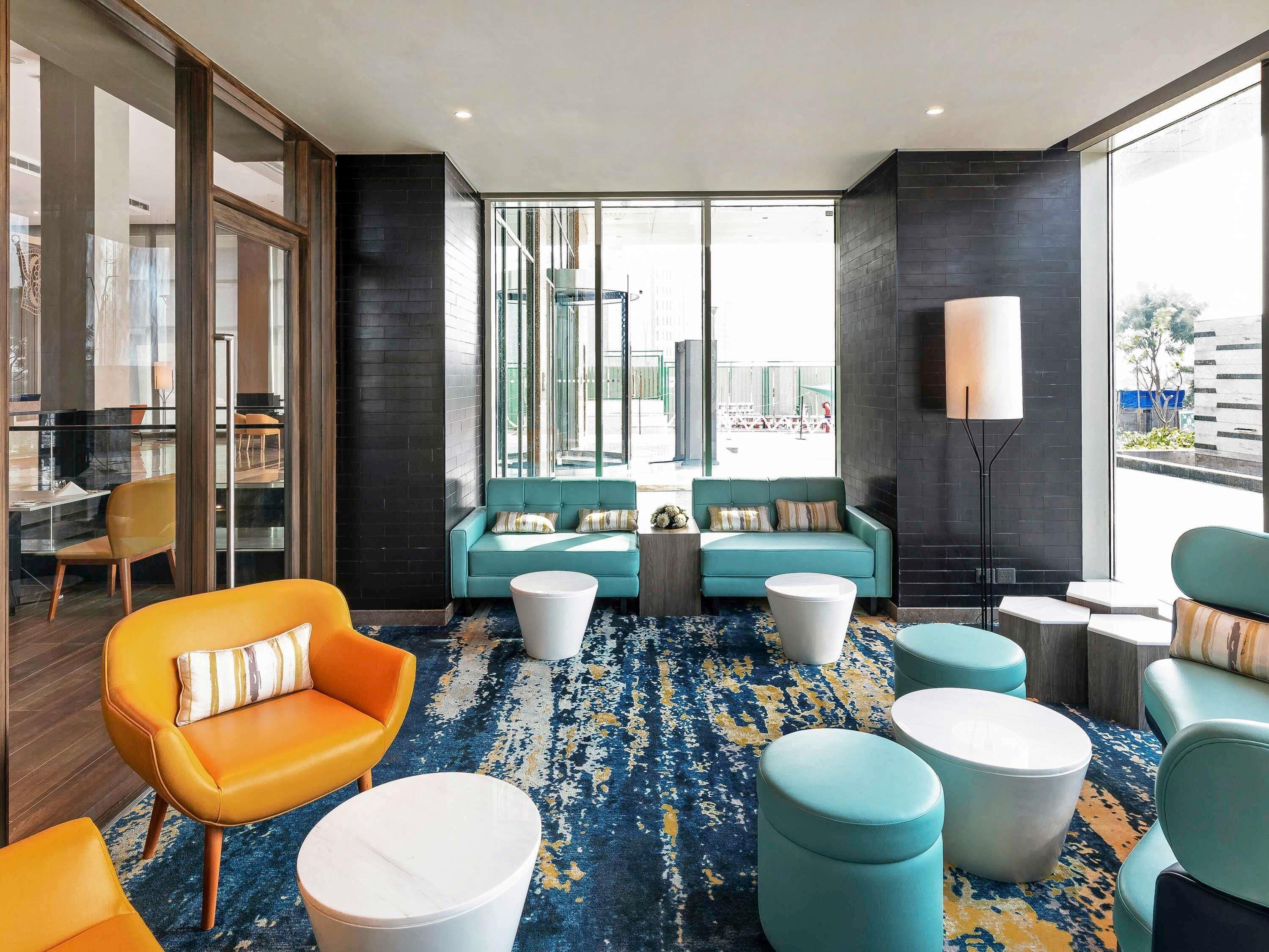 A modern lounge area with teal sofas, orange armchairs, and white round tables.