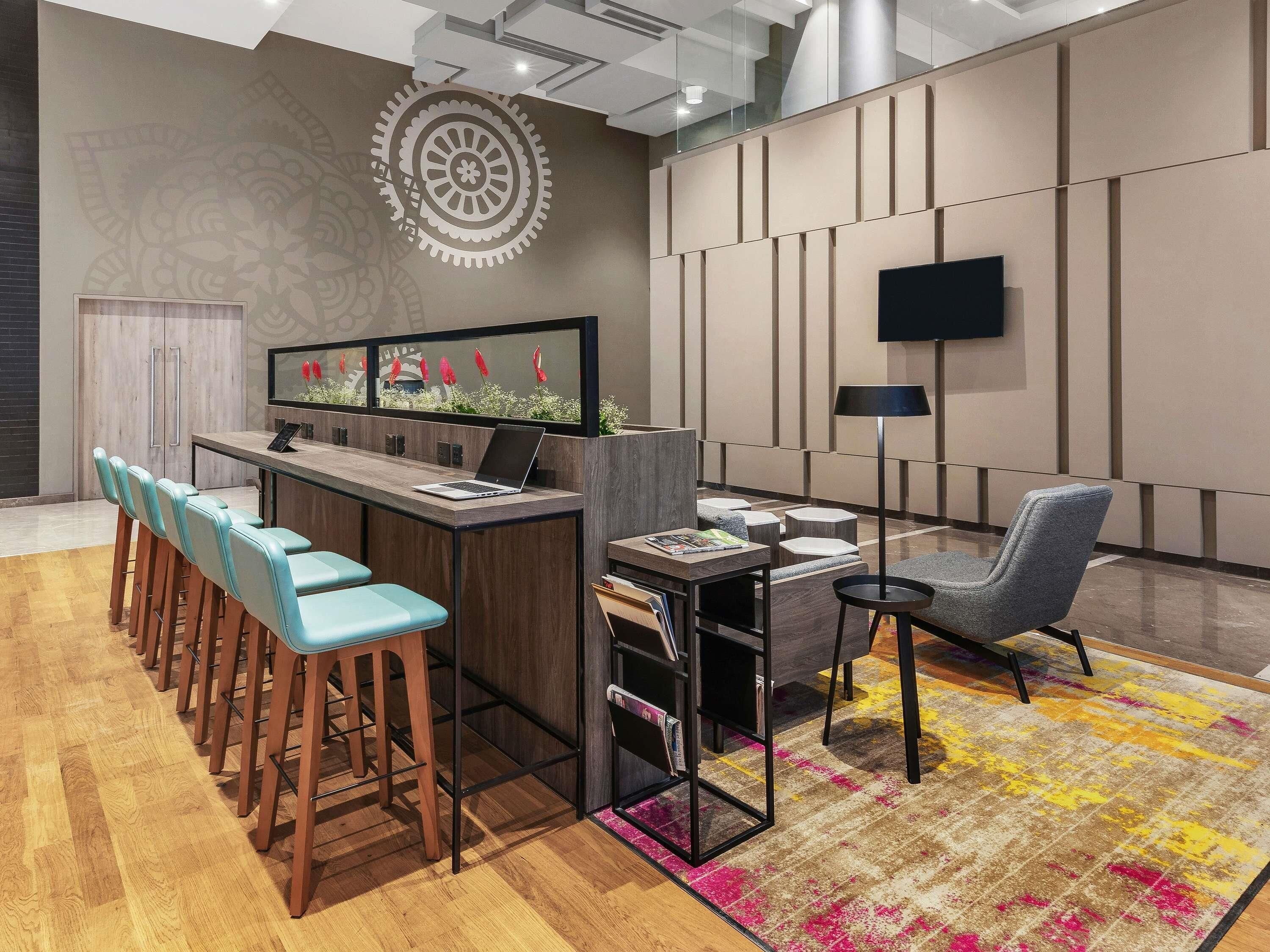 A modern bar area with a laptop, bar stools, a flat-screen TV, and a patterned rug.
