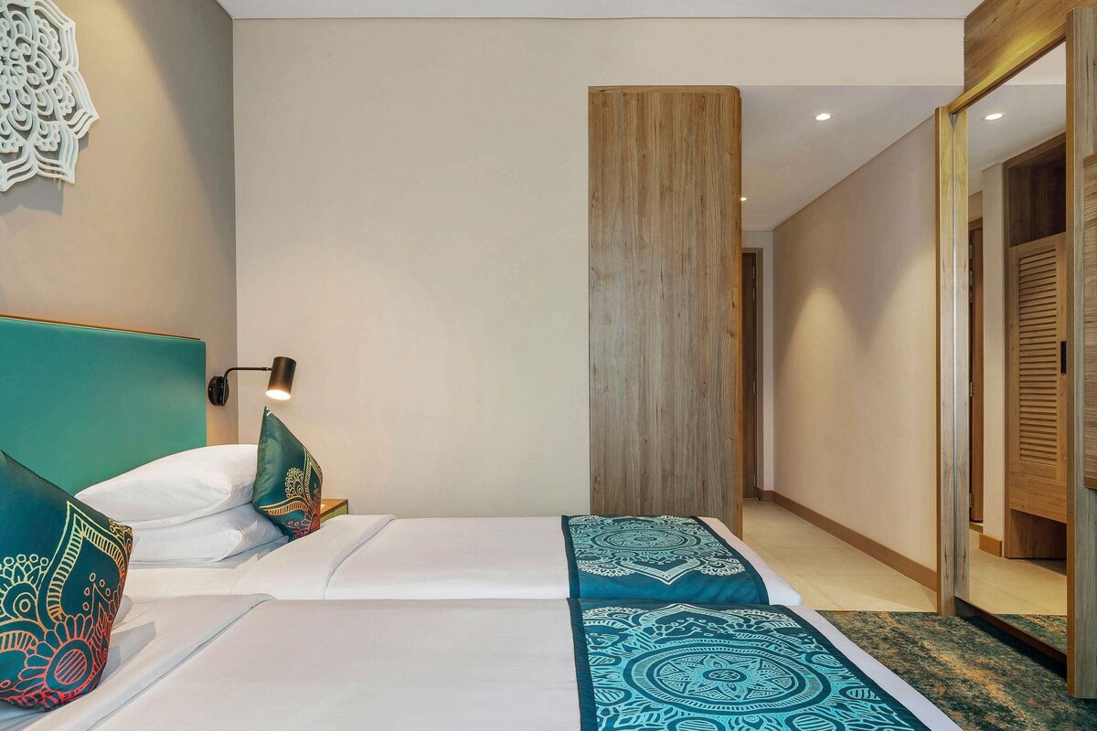 A hotel room with two beds, a wooden wardrobe, and a wall-mounted decorative piece.
