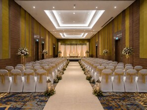 A hotel conference room with rows of chairs, a stage with a backdrop, and a carpeted floor.