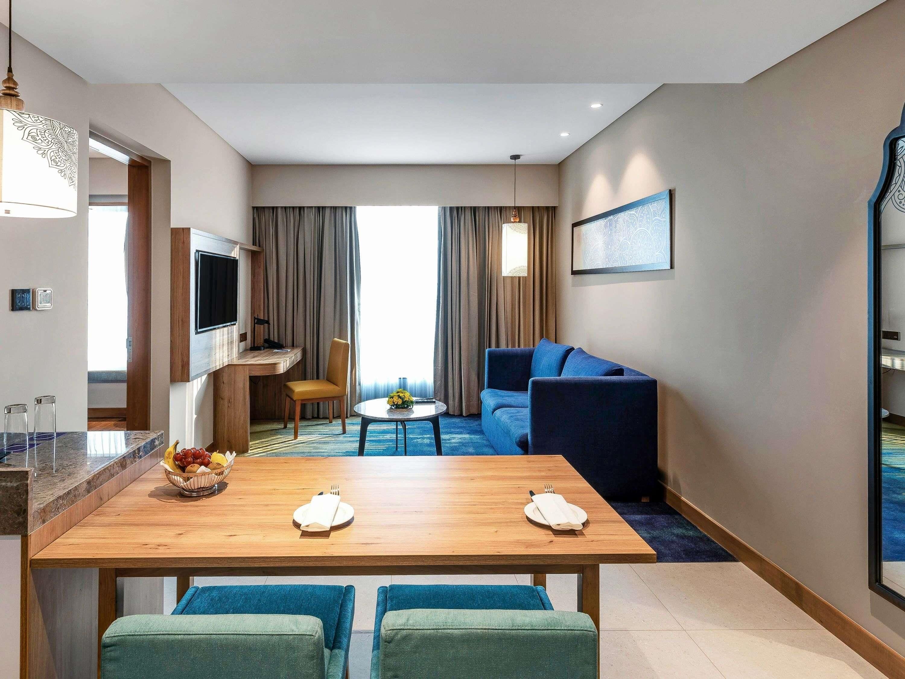 Een moderne hotelkamer met een zithoek, een bank, een televisie en een groot raam met gordijnen.