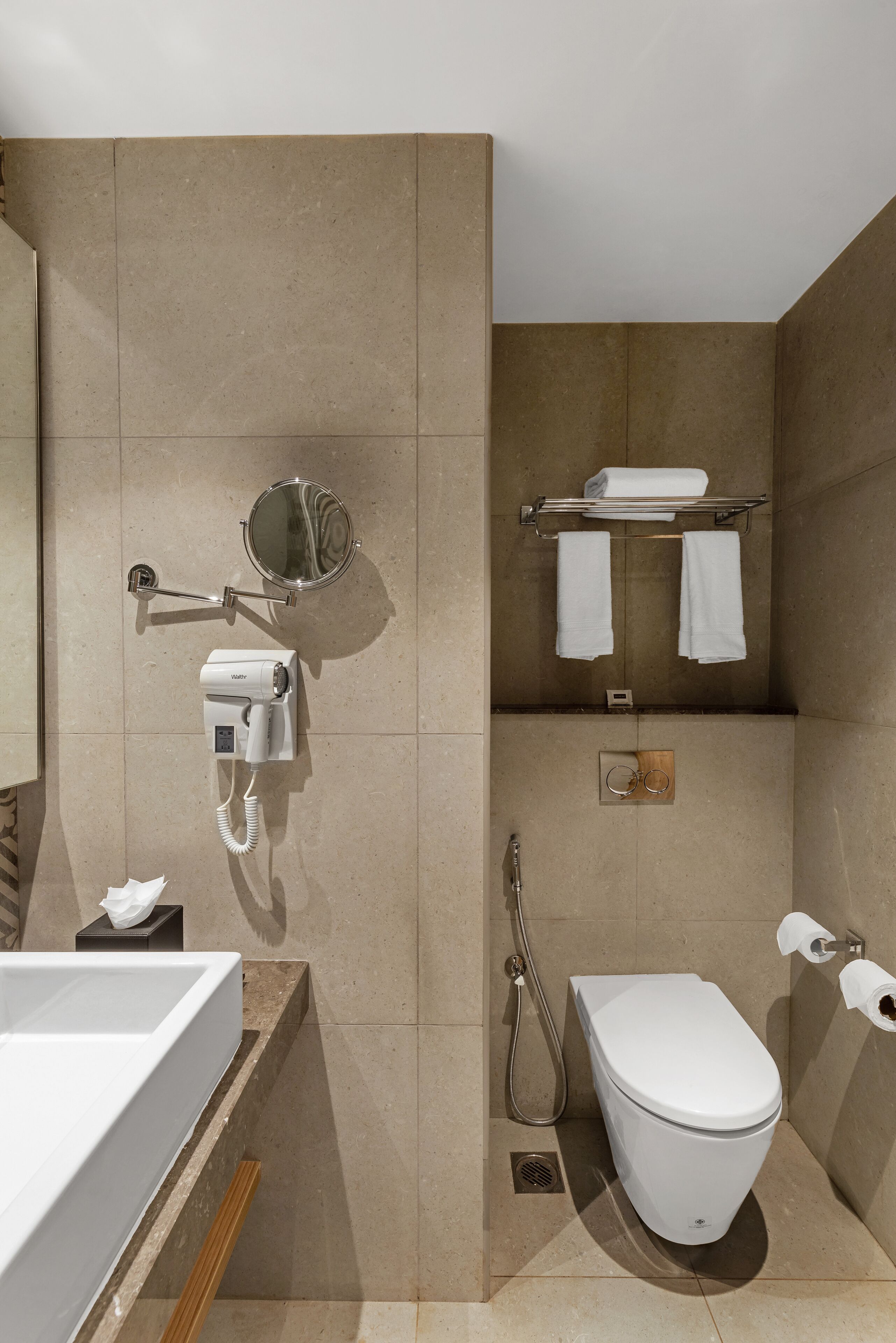 A modern bathroom with a white sink, a mirror, a hairdryer, a towel rack, a toilet, and a shower.