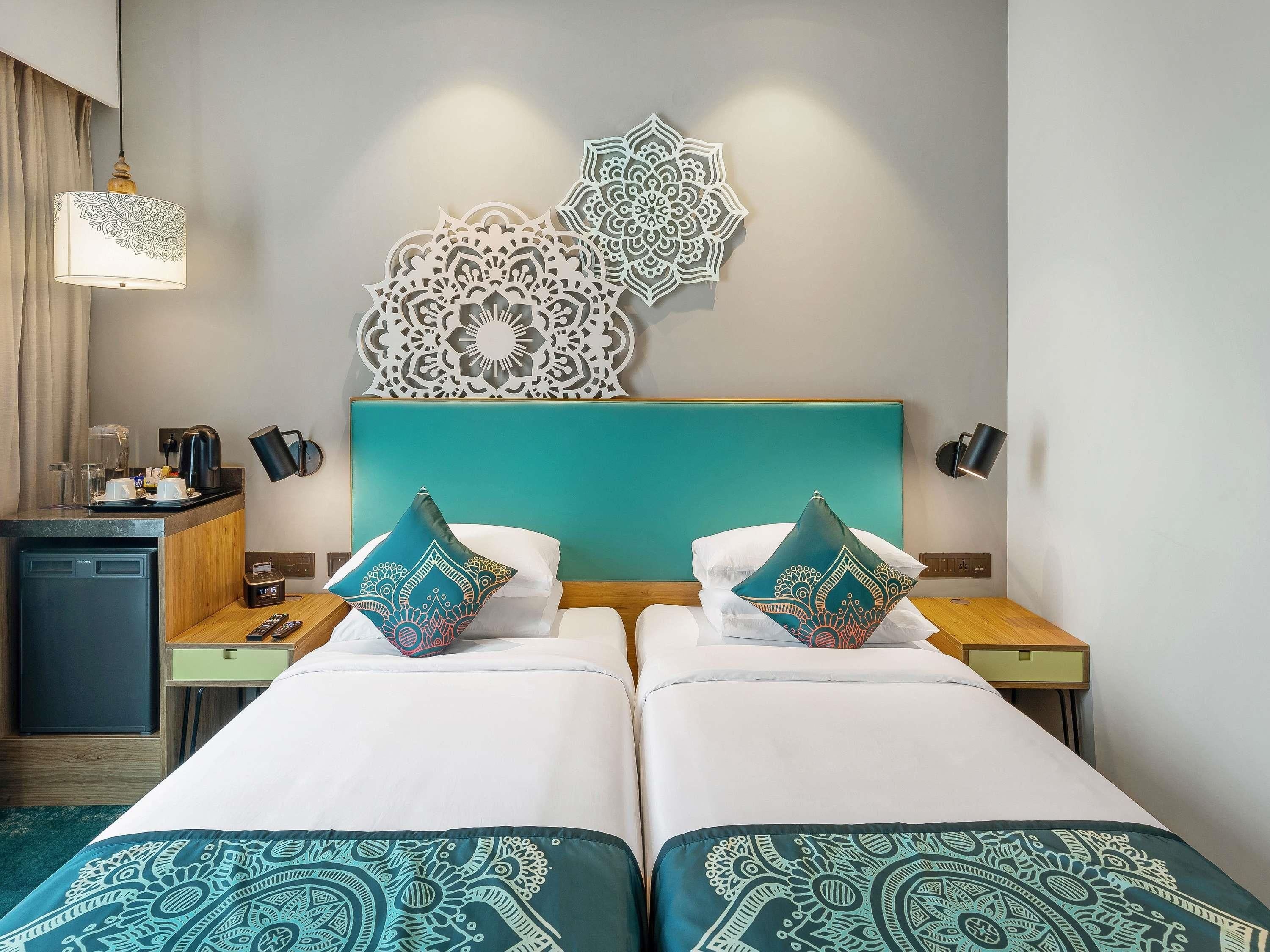 Habitación de hotel con dos camas, una kitchenette pequeña, detalles decorativos en la pared y una lámpara de noche.