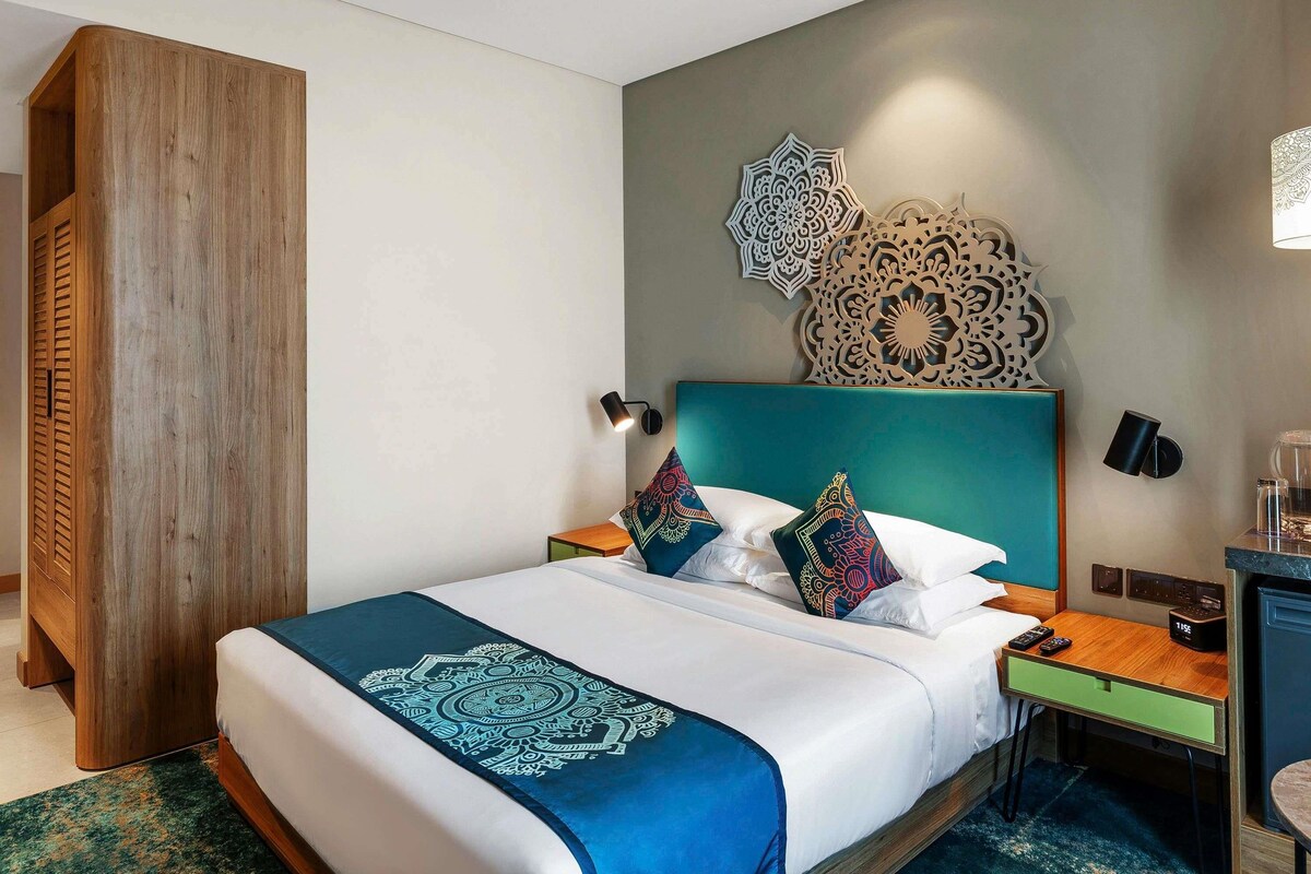 A hotel room with a bed, a nightstand, a desk, and decorative wall art.