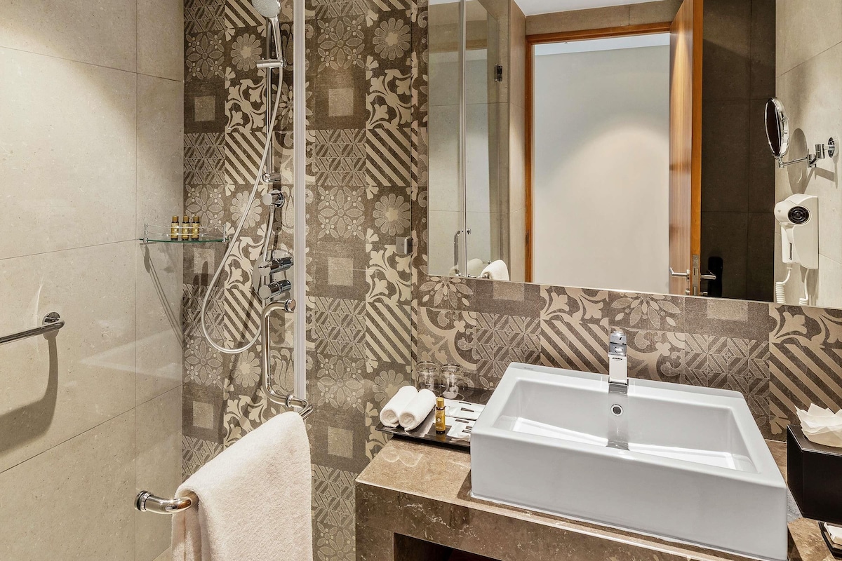 Un baño moderno con un lavamanos grande, ducha con cabezal de ducha manual y espejo con luz integrada.