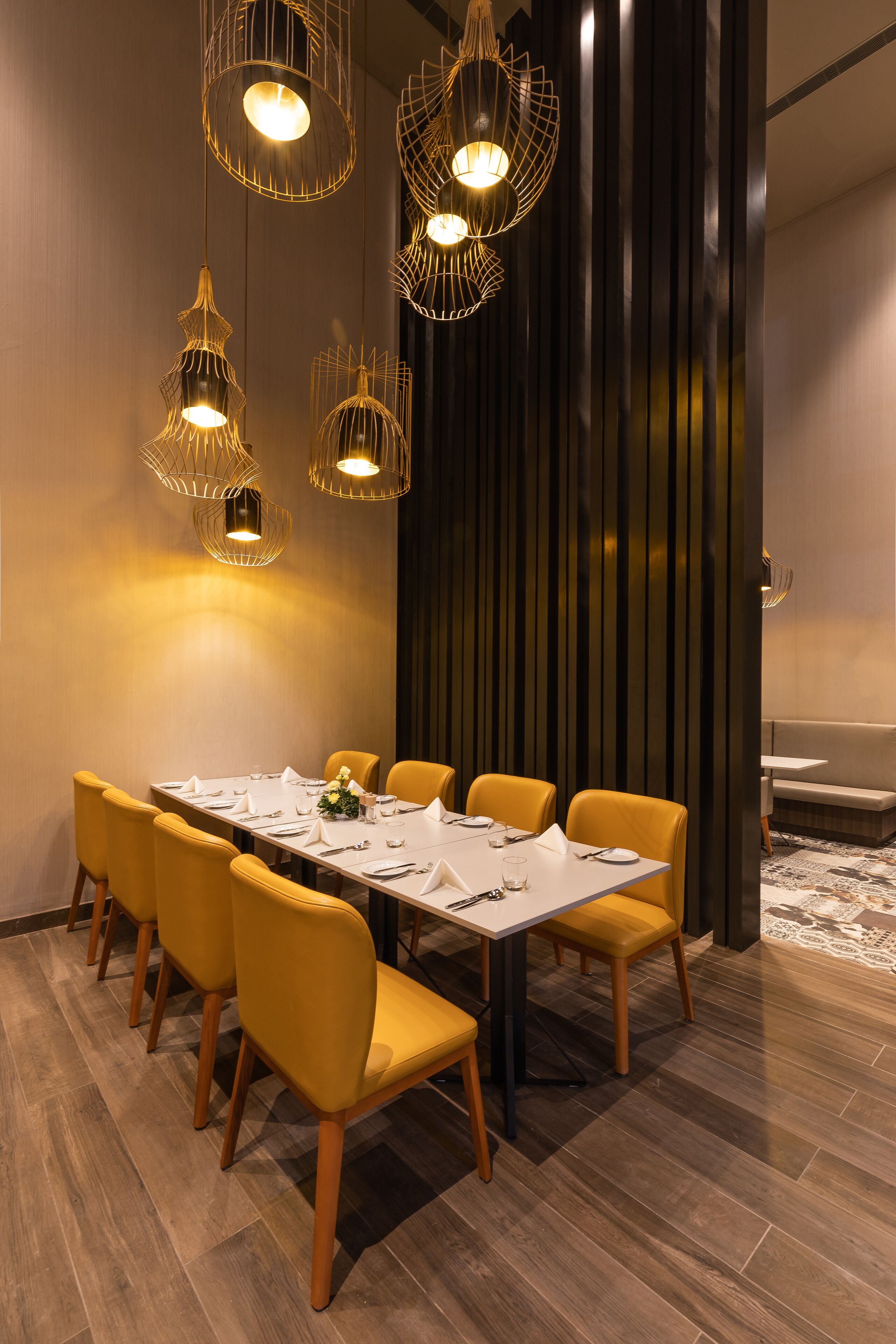 Un espace repas avec une longue table, des chaises jaunes et des lampes suspendues.