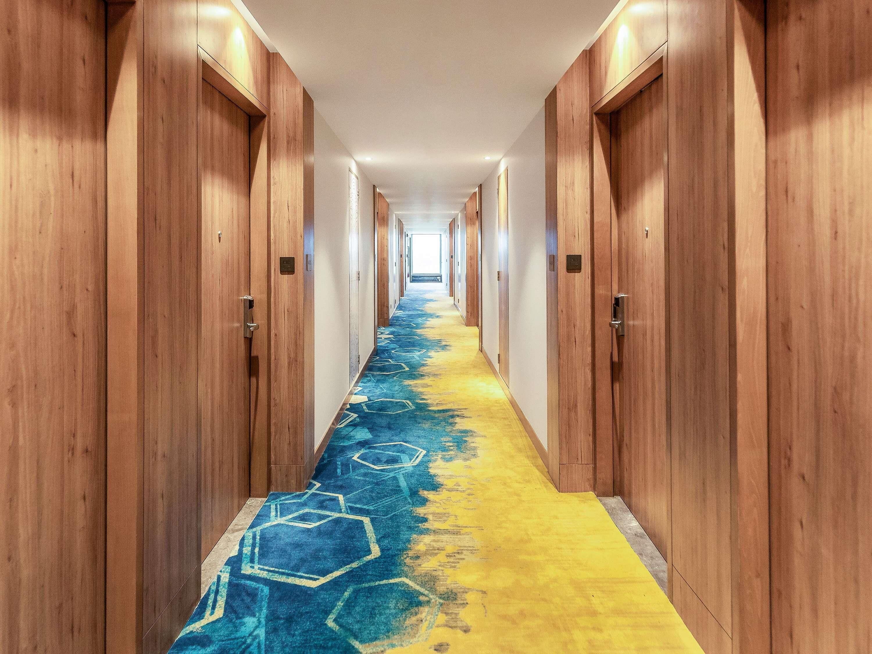 A hotel hallway with wooden doors, a patterned carpet, and a light-colored floor.