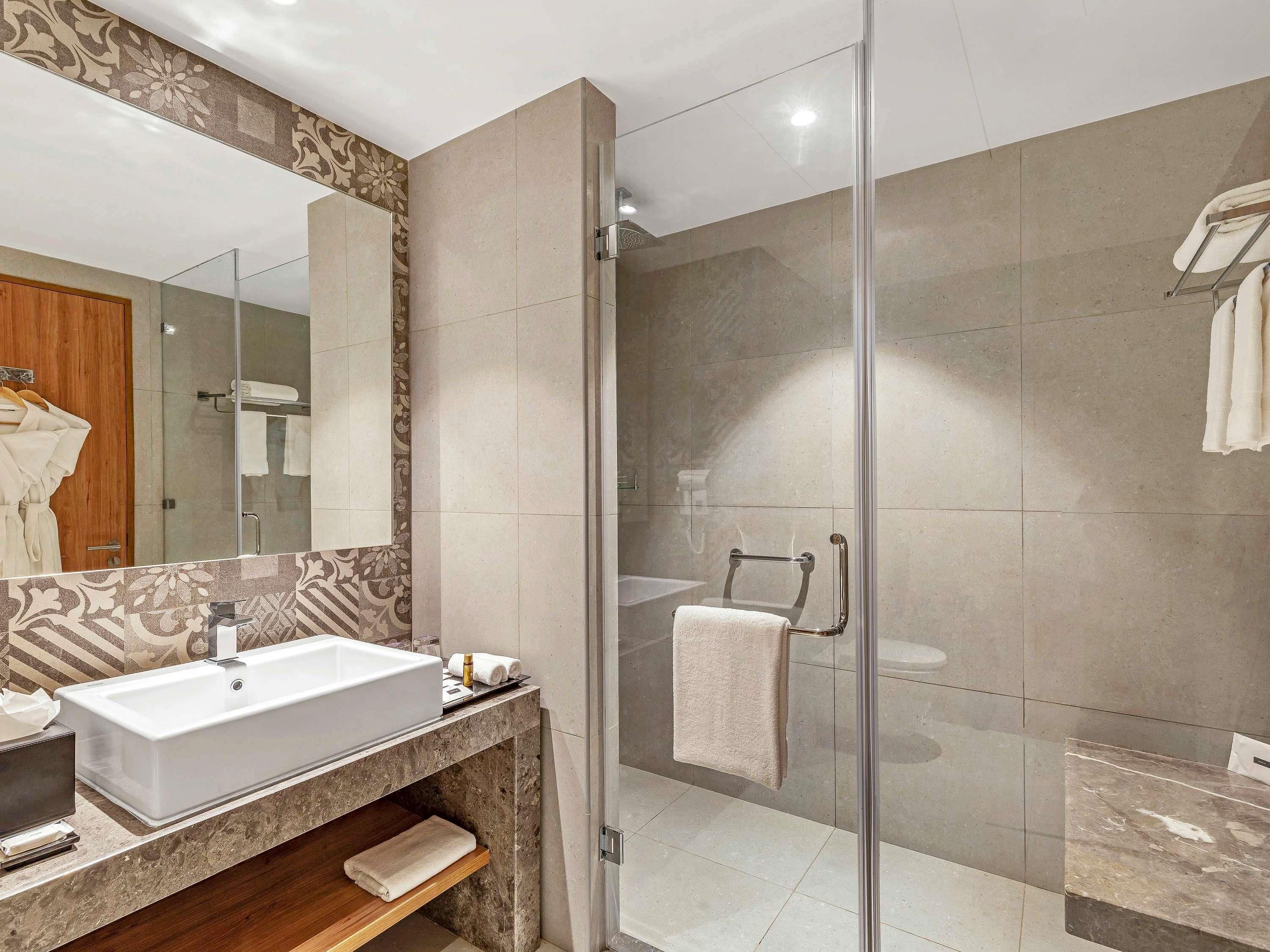 Un baño moderno con un lavamanos grande, una cabina de ducha con mampara de vidrio y un espejo con un detalle decorativo.