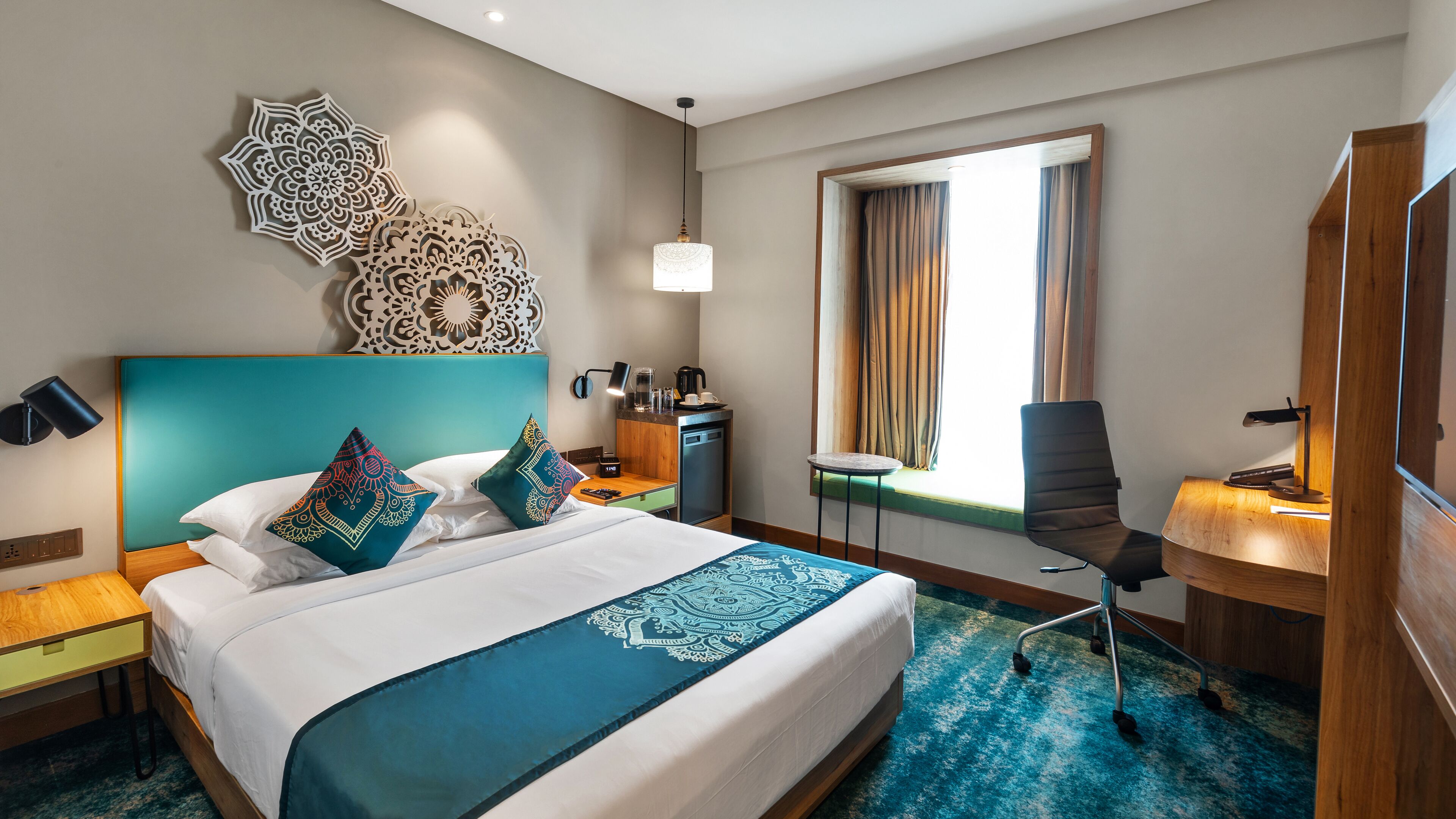 A hotel room with a large bed, a desk, a chair, a window with curtains, and a decorative wall piece.
