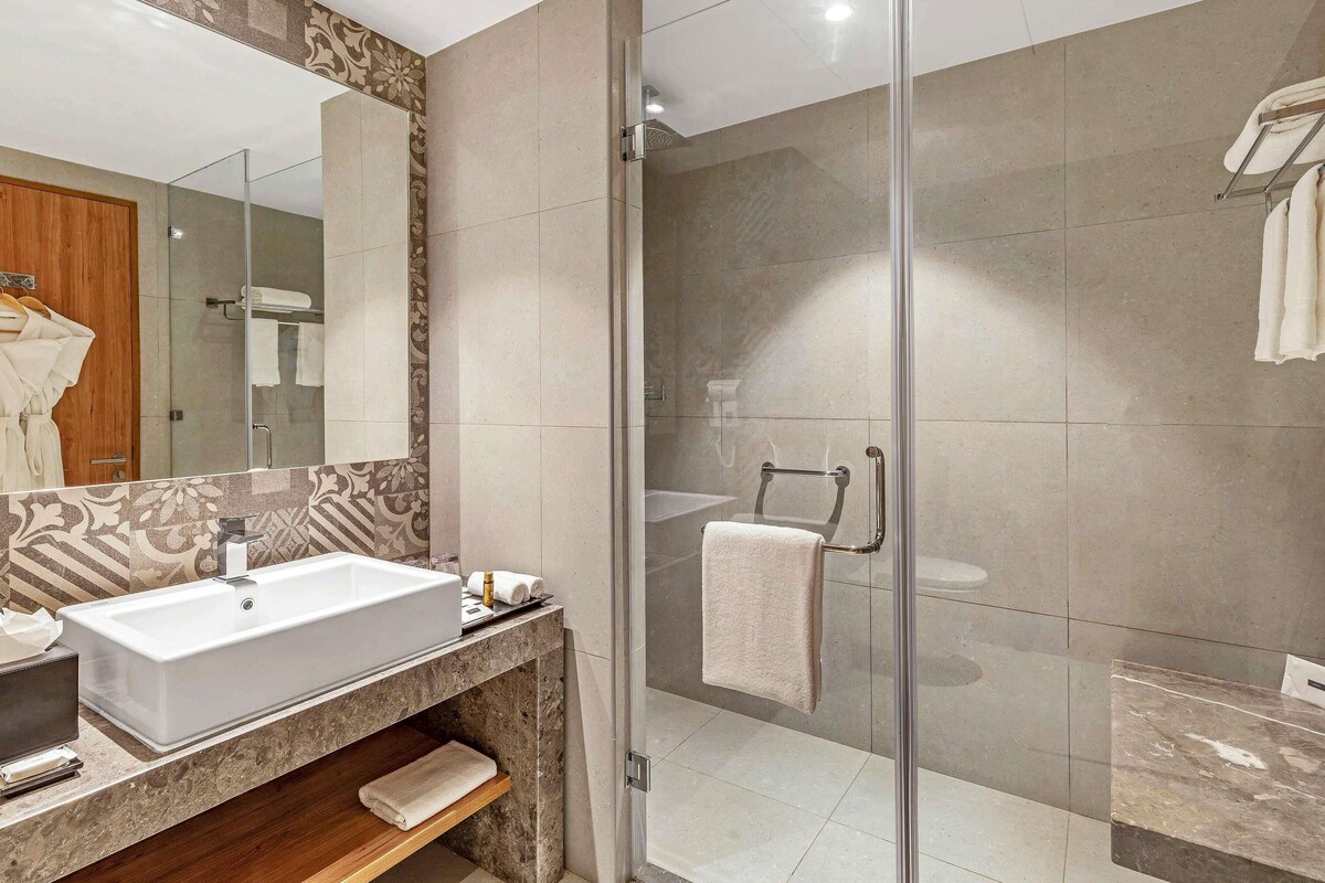Un baño moderno con un lavamanos grande, una cabina de ducha con mampara de vidrio y un espejo con un detalle decorativo.