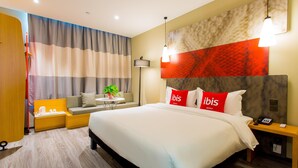 Una habitación de hotel con una cama grande, un sofá, una mesita con una planta y una mesita de noche con un teléfono.