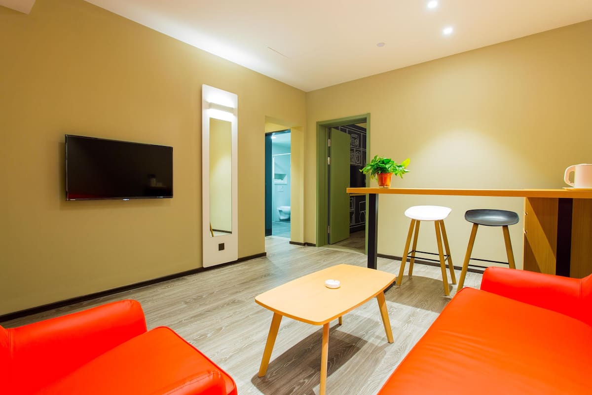 Quarto moderno com televisão, uma pequena mesa, duas cadeiras e um banco.