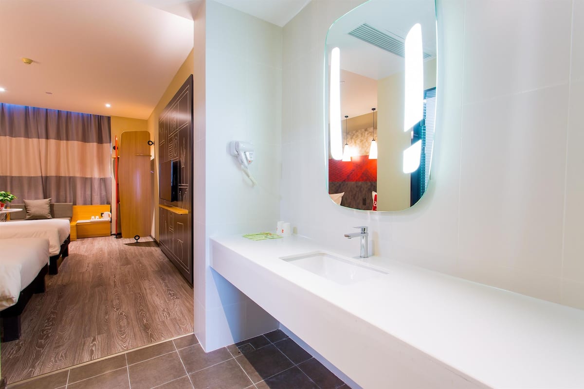 Quarto de hotel moderno com uma cama grande, um espaço de estar separado, um banheiro com um espelho grande e pia, e um quarto separado.