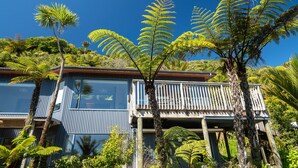 En moderne bygning med balkon, omgivet af frodig vegetation, herunder bregner og palmer.