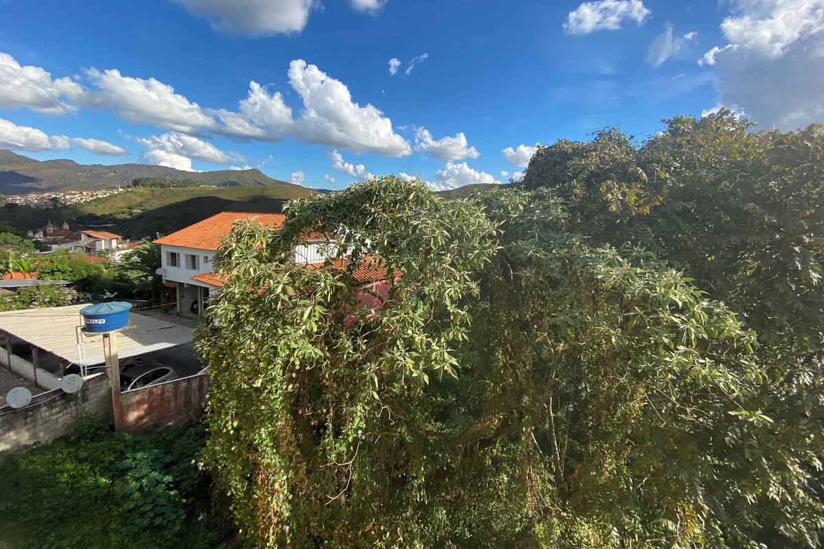 Ein Wohngebiet mit einem Haus mit rotem Ziegeldach, umgeben von üppiger Vegetation und Hügeln im Hintergrund.