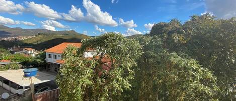 A residential area with a house featuring a red-tiled roof, surrounded by lush greenery and hills in the background.