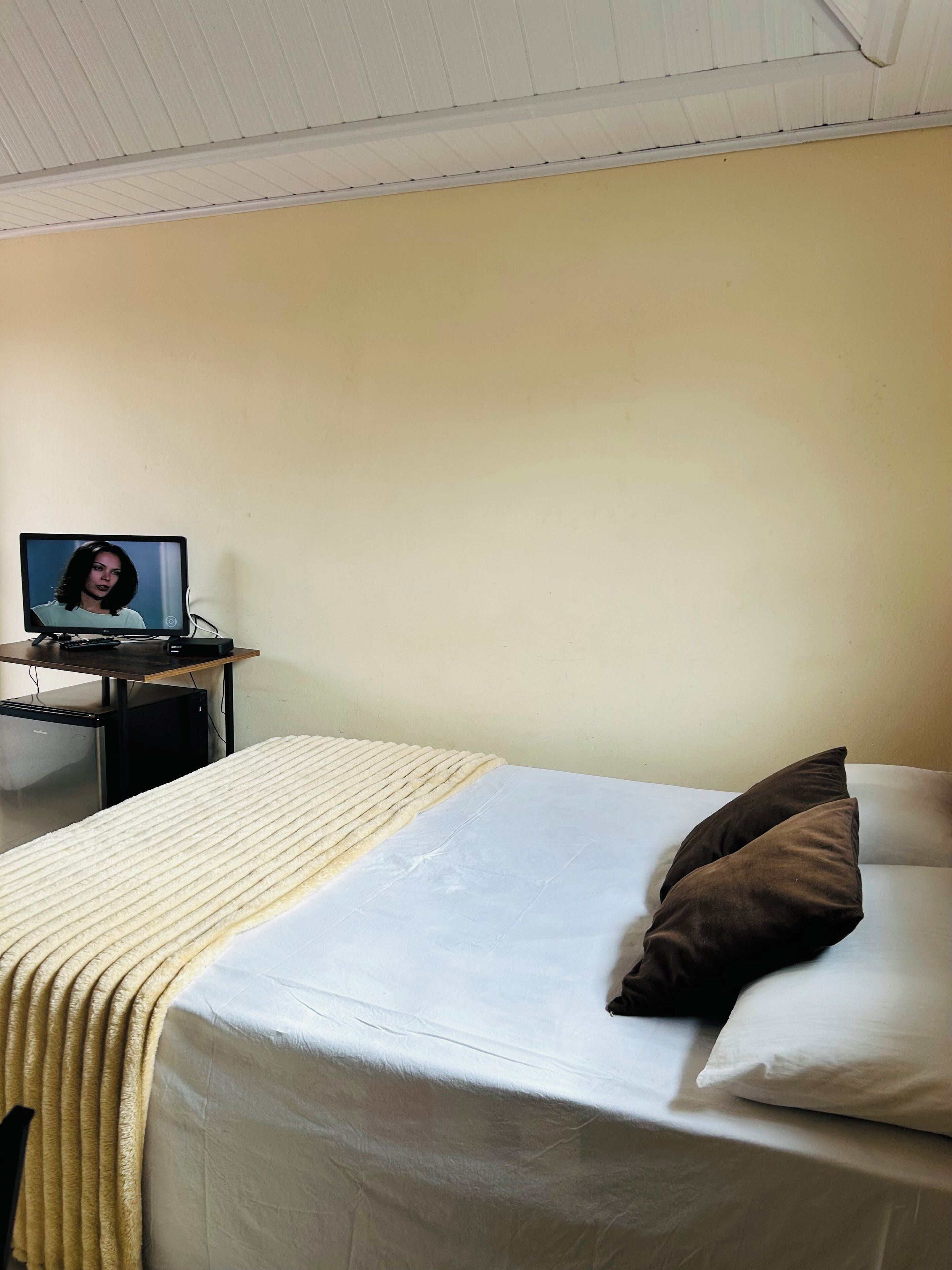 Een hotelkamer met een bed, een bureau met een laptop en een kleine koelkast.