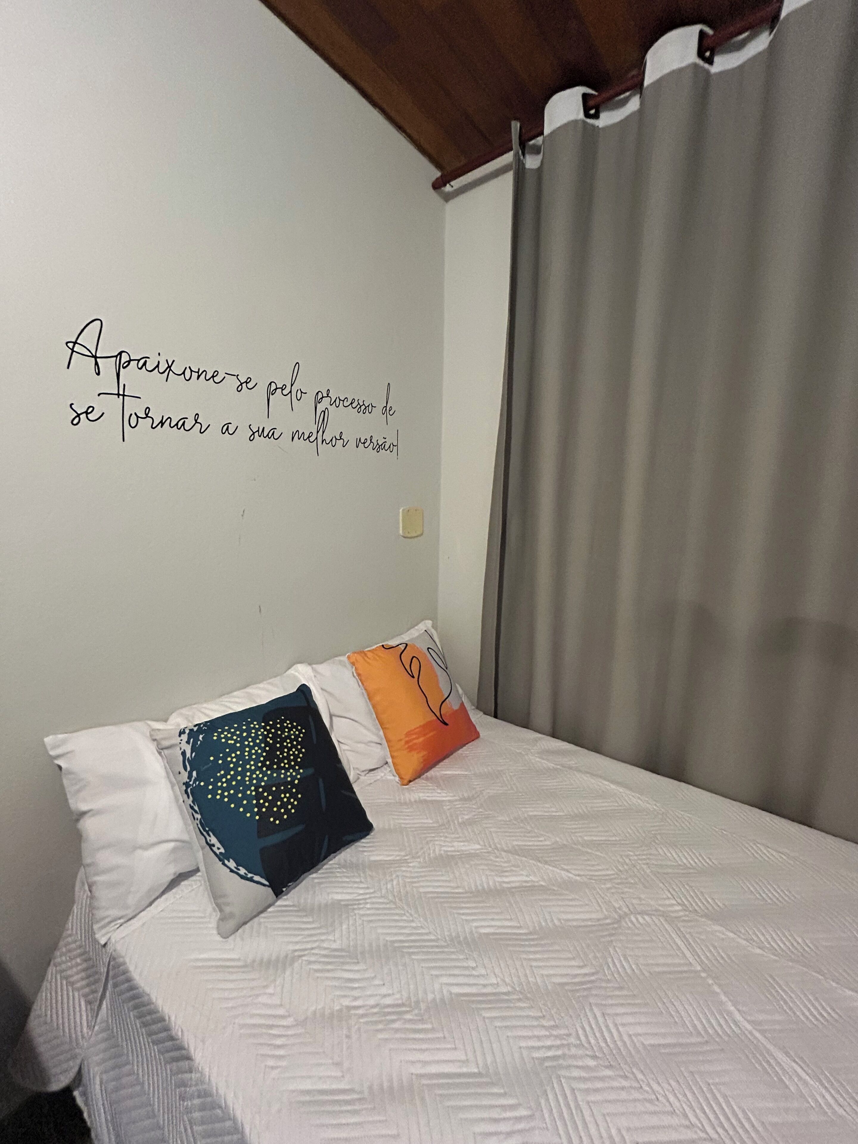 Un lit bien fait, avec une literie à motifs, un mur orné d’une citation inspirante et un rideau.