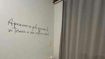 Un lit bien fait, avec une literie à motifs, un mur orné d’une citation inspirante et un rideau.