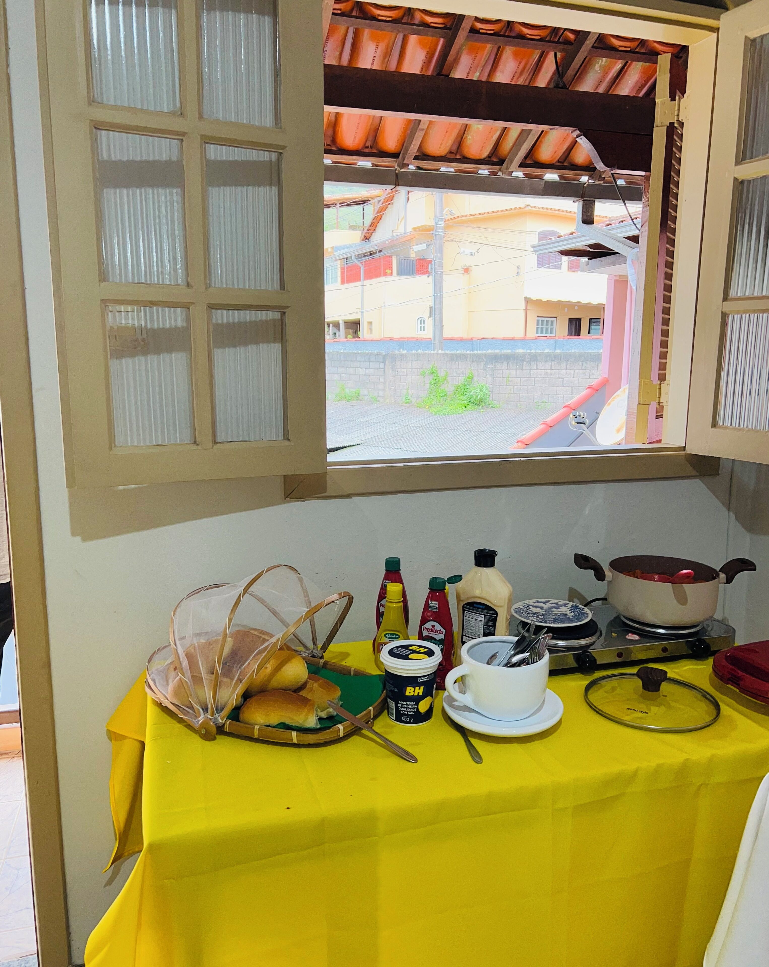A table with breakfast items, a window with a view of buildings, and a yellow tablecloth.