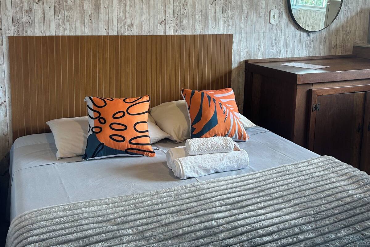 Ein ordentlich bezogenes Bett mit einer gestreiften Decke, einem Holz-Kopfteil und zwei Kissen mit Tiger-Motiv.