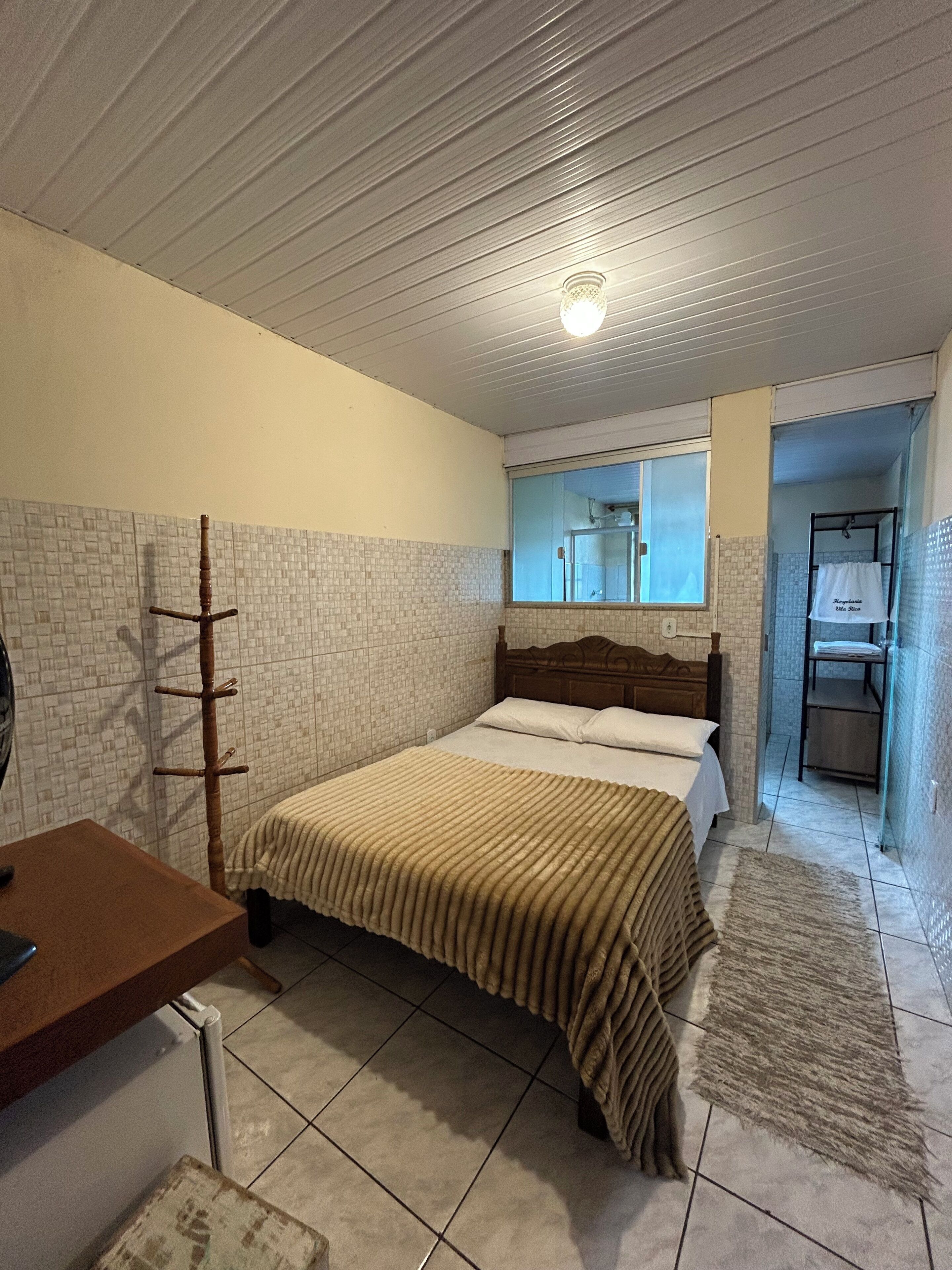 A bedroom with a bed, a wooden chair, a small table, and a mirror.