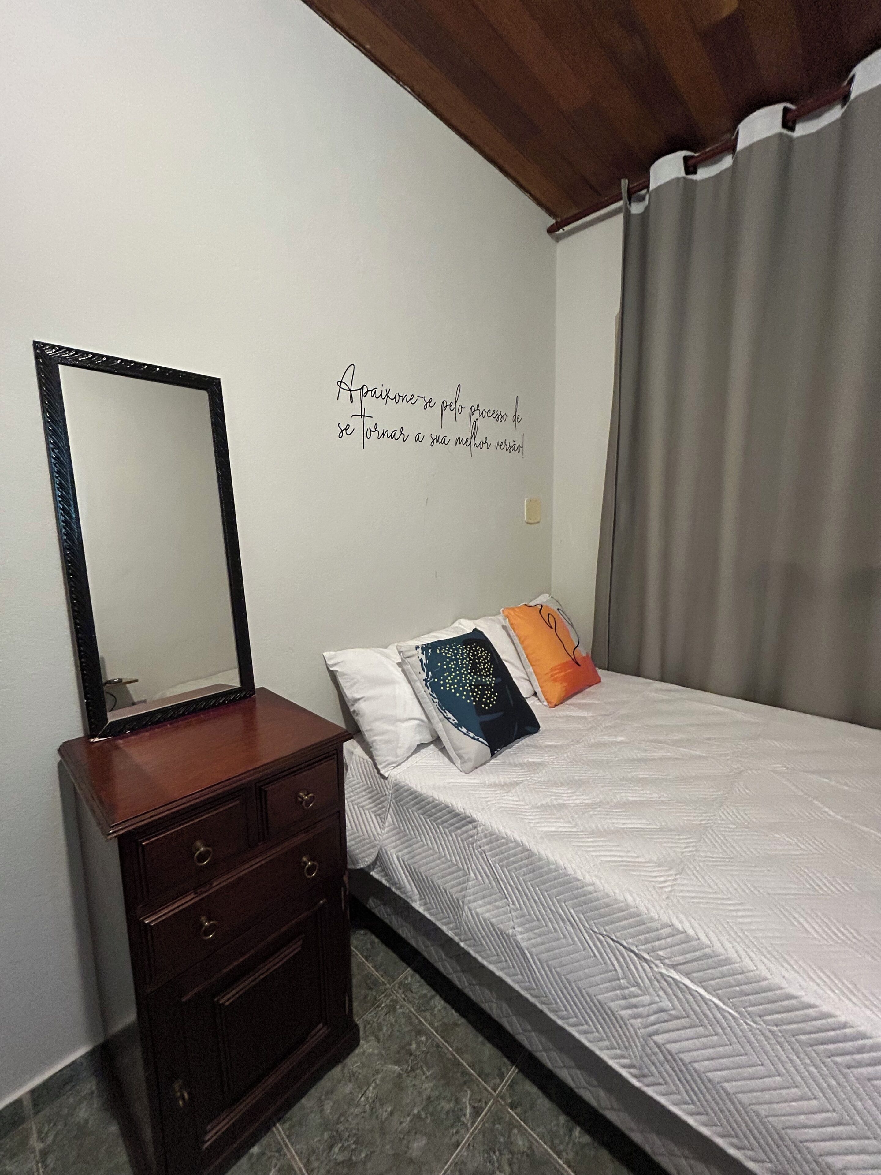 A bedroom with a bed, a dresser, a mirror, and a wall with a motivational quote.