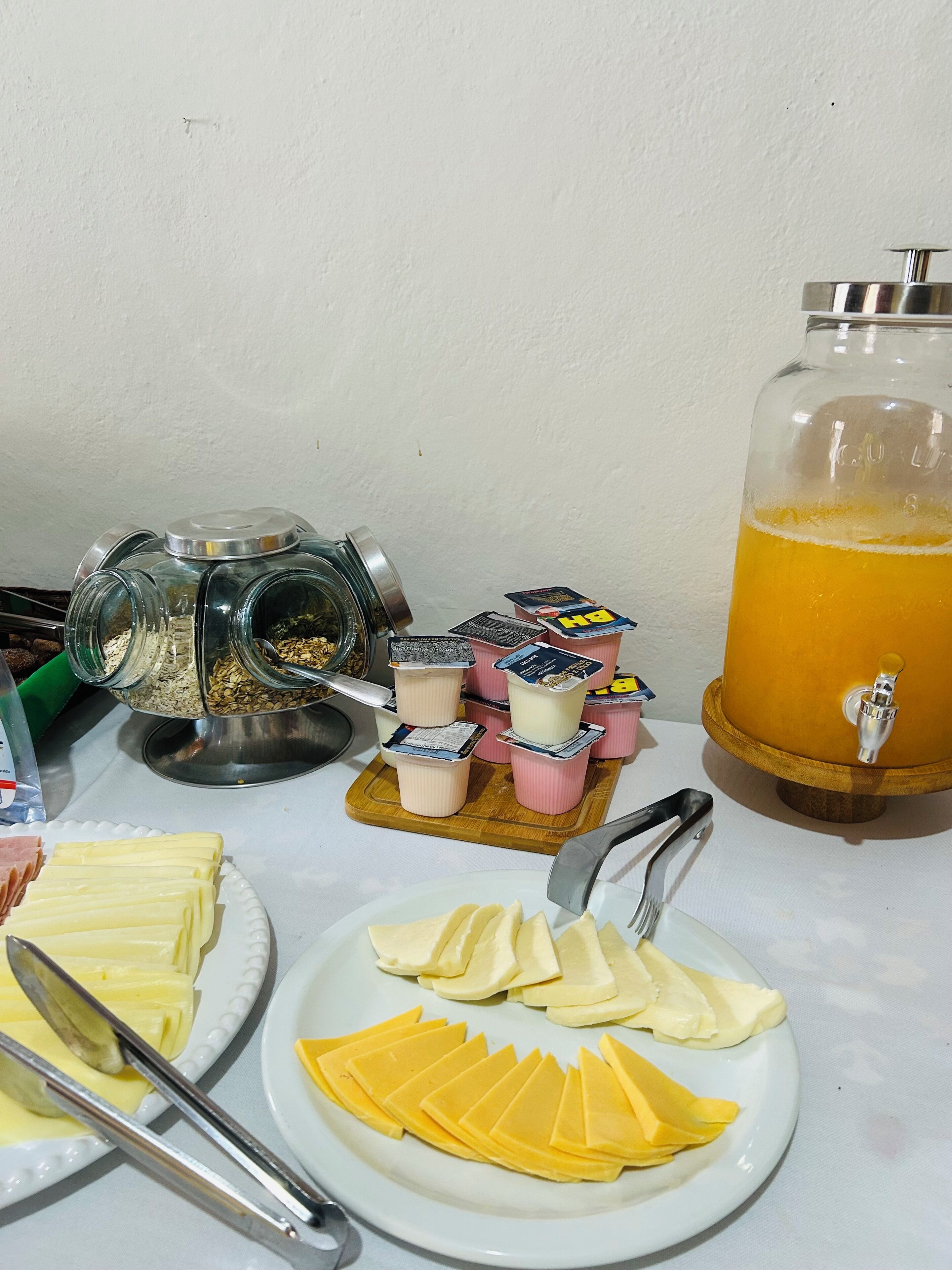 En morgenmadsanretning med yoghurtkopper, skiver af ost og et stort glas appelsinjuice.