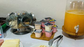 Preparación para el desayuno con vasos de yogur, rebanadas de queso y un vaso grande de jugo de naranja.