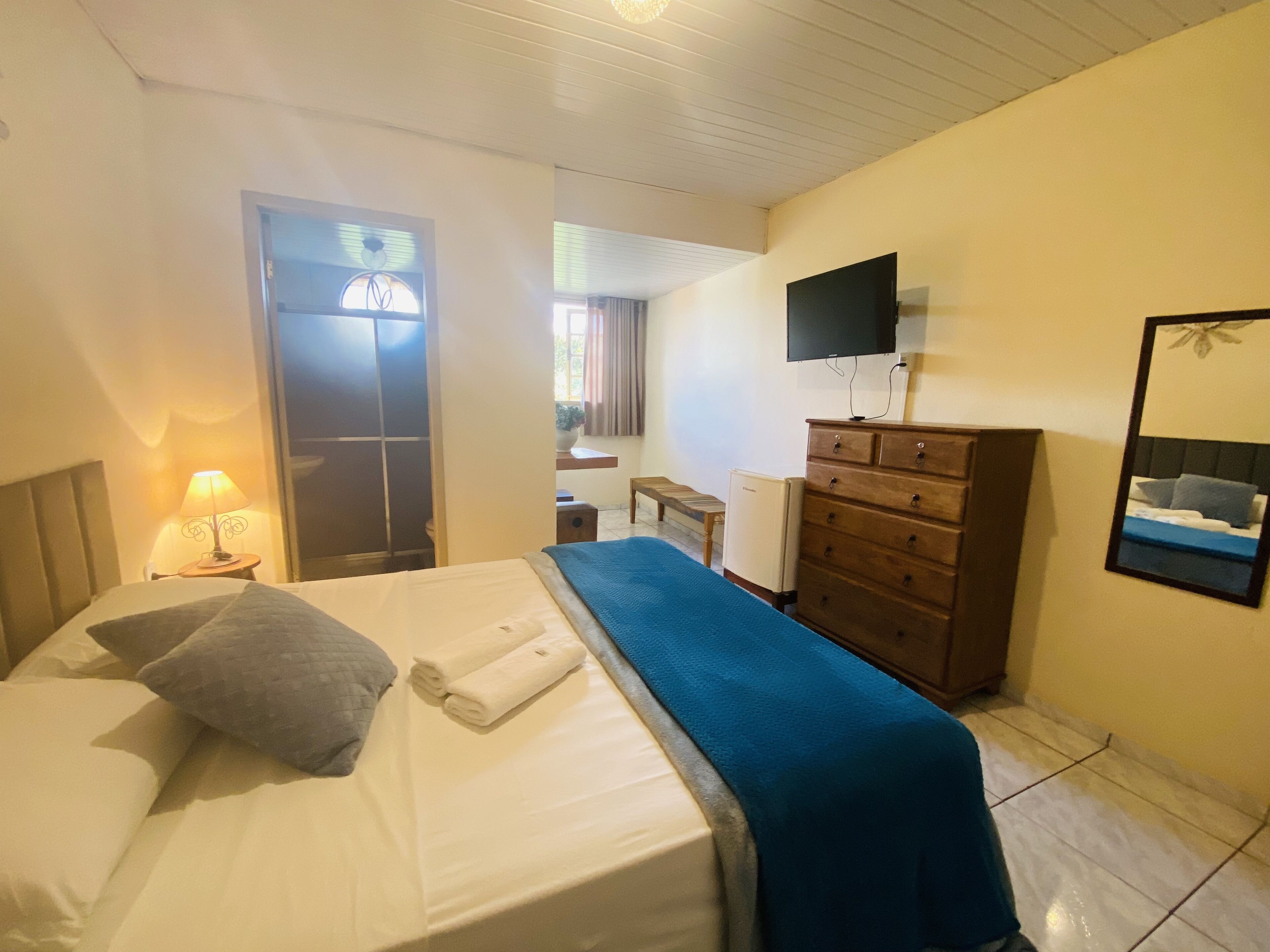 Une chambre d’hôtel avec un lit, une commode, une télévision et une fenêtre avec des stores.
