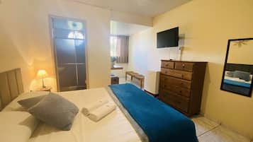 Habitación de hotel con cama, cómoda, televisor y ventana con persianas.