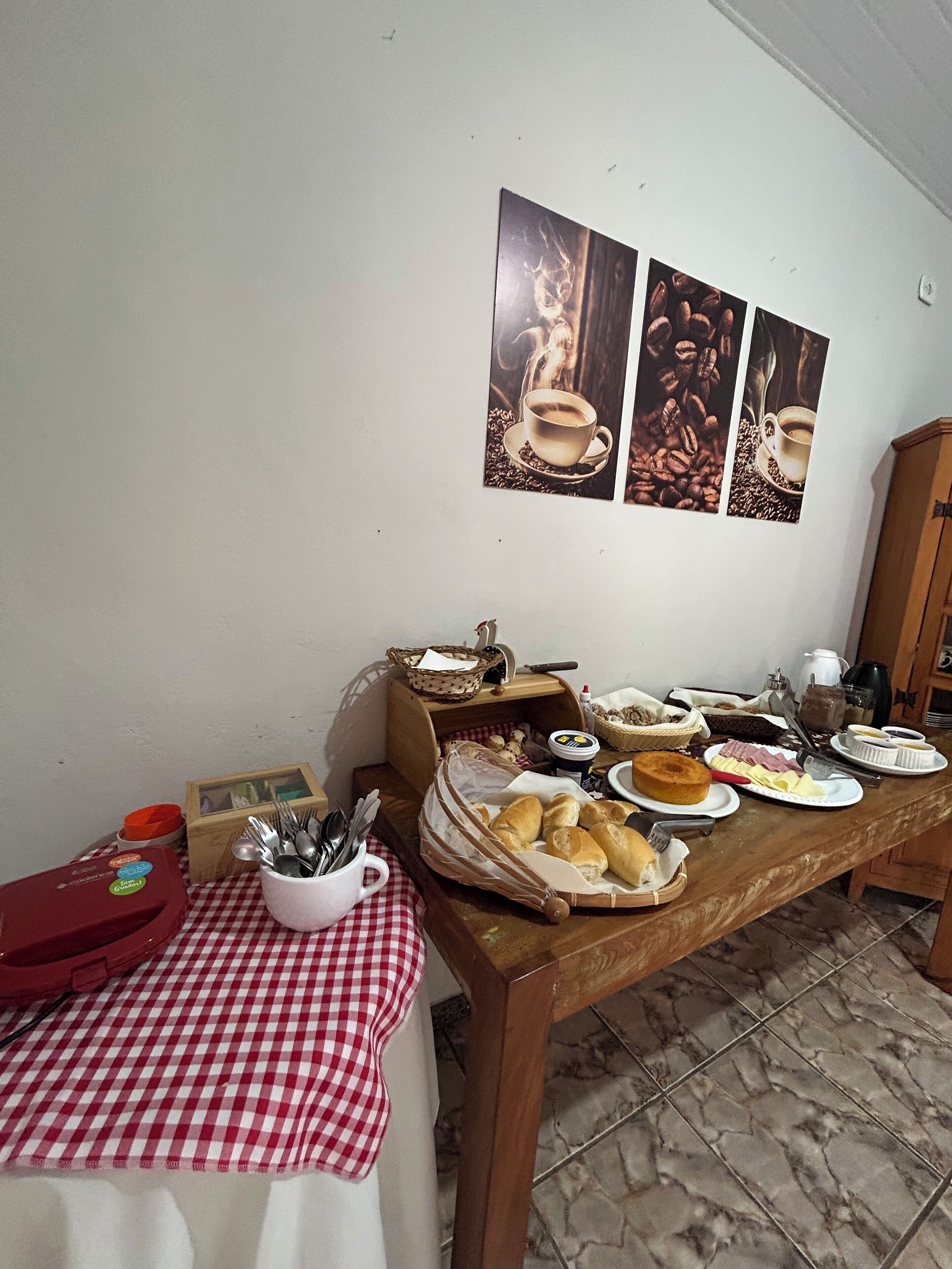 A dining table set with various food items and a coffee cup, a basket of bread, and a red container.