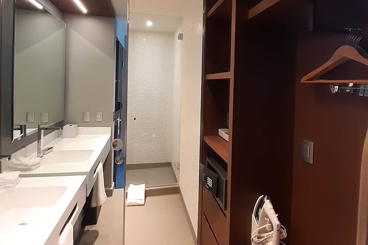 Un baño moderno con lavamanos dobles, un espejo grande, cabina de ducha y tocador de madera con un bolso colgando.