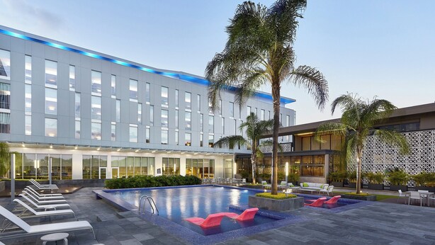 Un hotel moderno con piscina, tumbonas y palmeras.
