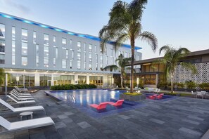 Un hotel moderno con piscina, tumbonas y palmeras.