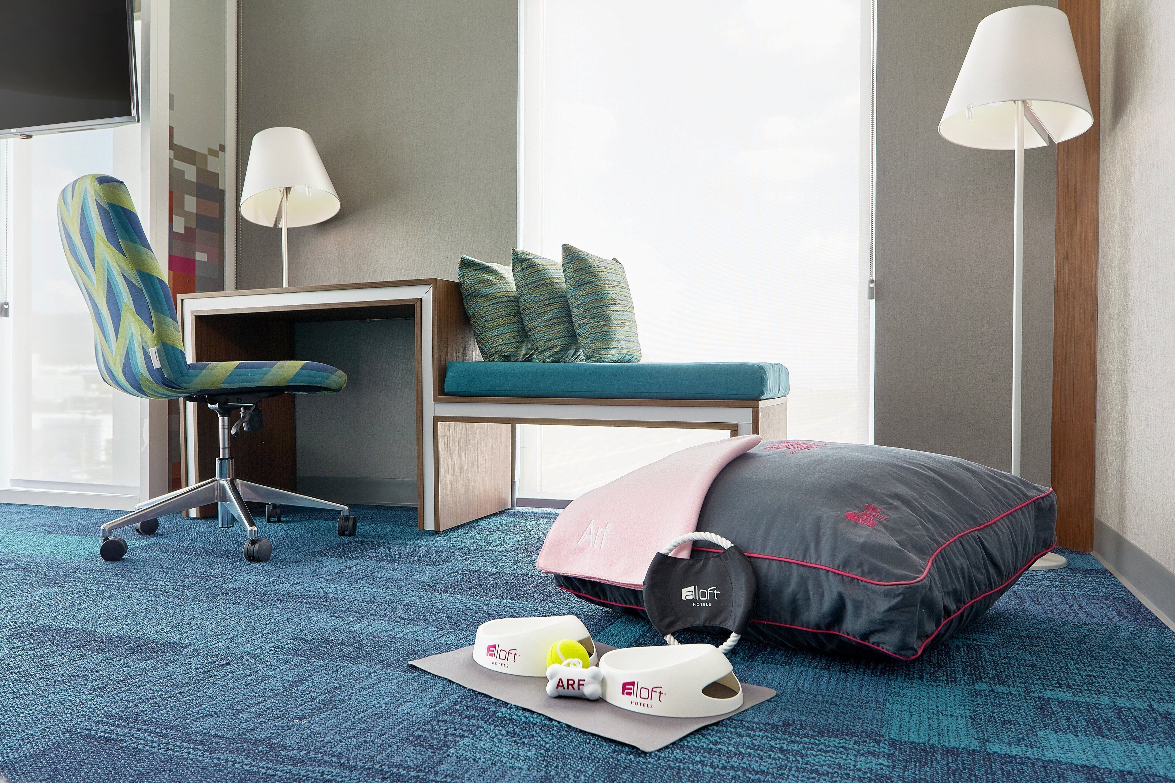 Hotellihuone, jossa on työpöytä, tuoli, sängyssä tyyny, yöpöytä ja lamppu.