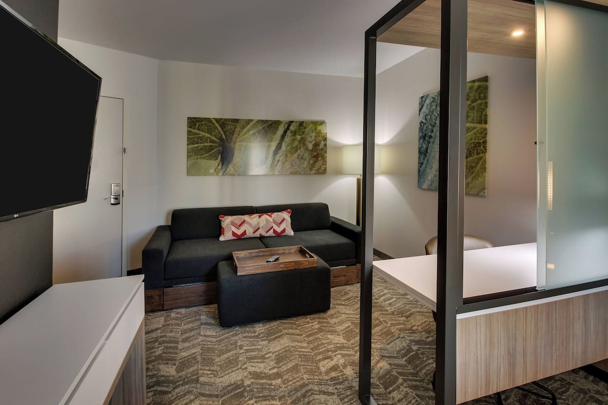 Ein modernes Hotelzimmer mit einer Couch, einem Hocker und einem Flachbildfernseher.