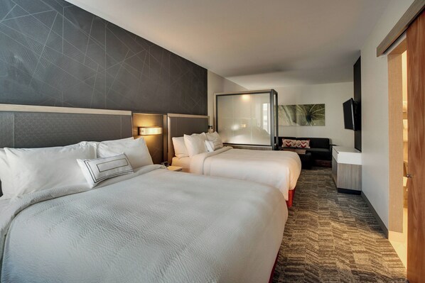 A hotel room with two beds, a desk, a TV, and a large window.