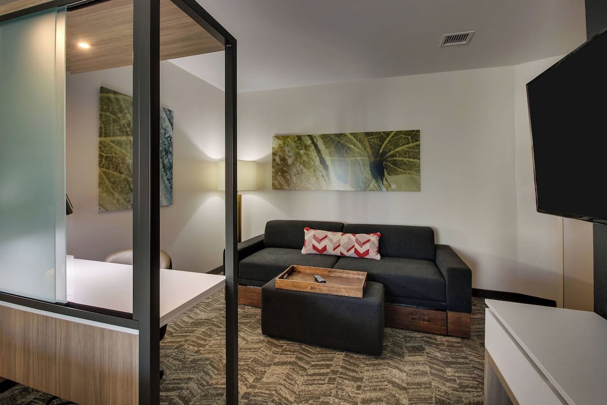 Ein modernes Hotelzimmer mit einer Couch, einem Holztisch, einem Flachbildfernseher und Kunstwerken an den Wänden.