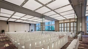 A large, well-lit room with rows of white chairs, large windows, and a patterned carpet.