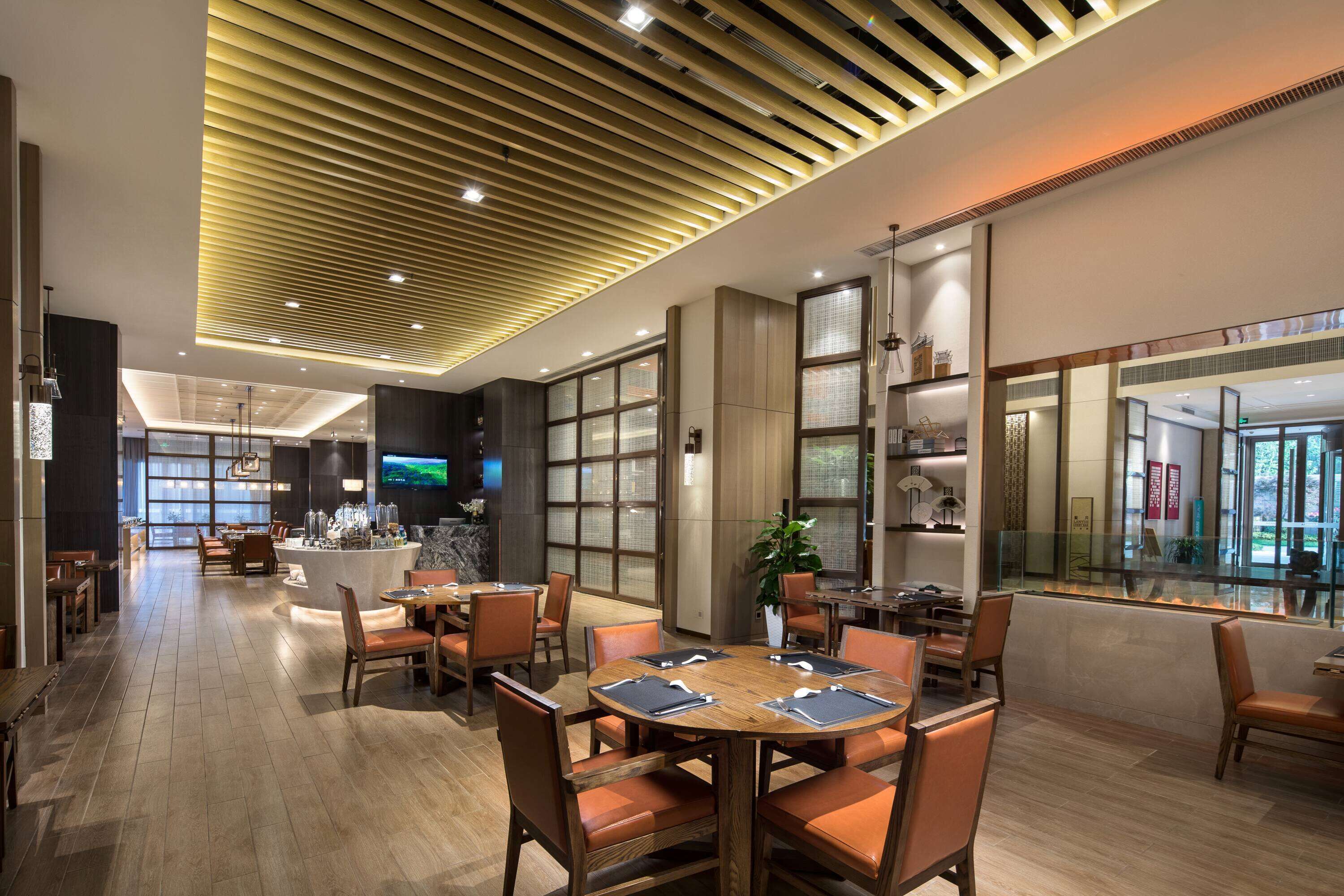 Un moderno vestíbulo de hotel con techo de madera, una zona de bar y diferentes disposiciones de asientos.