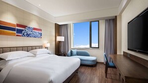 Habitación de hotel con una cama grande, un escritorio, un televisor y una ventana con vistas al cielo.