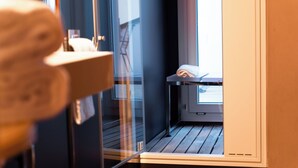 A modern hotel room with a wooden floor, a glass door leading to a balcony, and a neatly made bed. - Casa d'Este - Hotel Ferrara (Ferrara)
