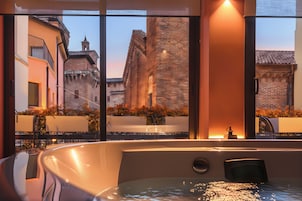 Un baño moderno con una bañera grande, una ventana que ofrece vistas a edificios históricos y una pequeña zona con lavamanos.