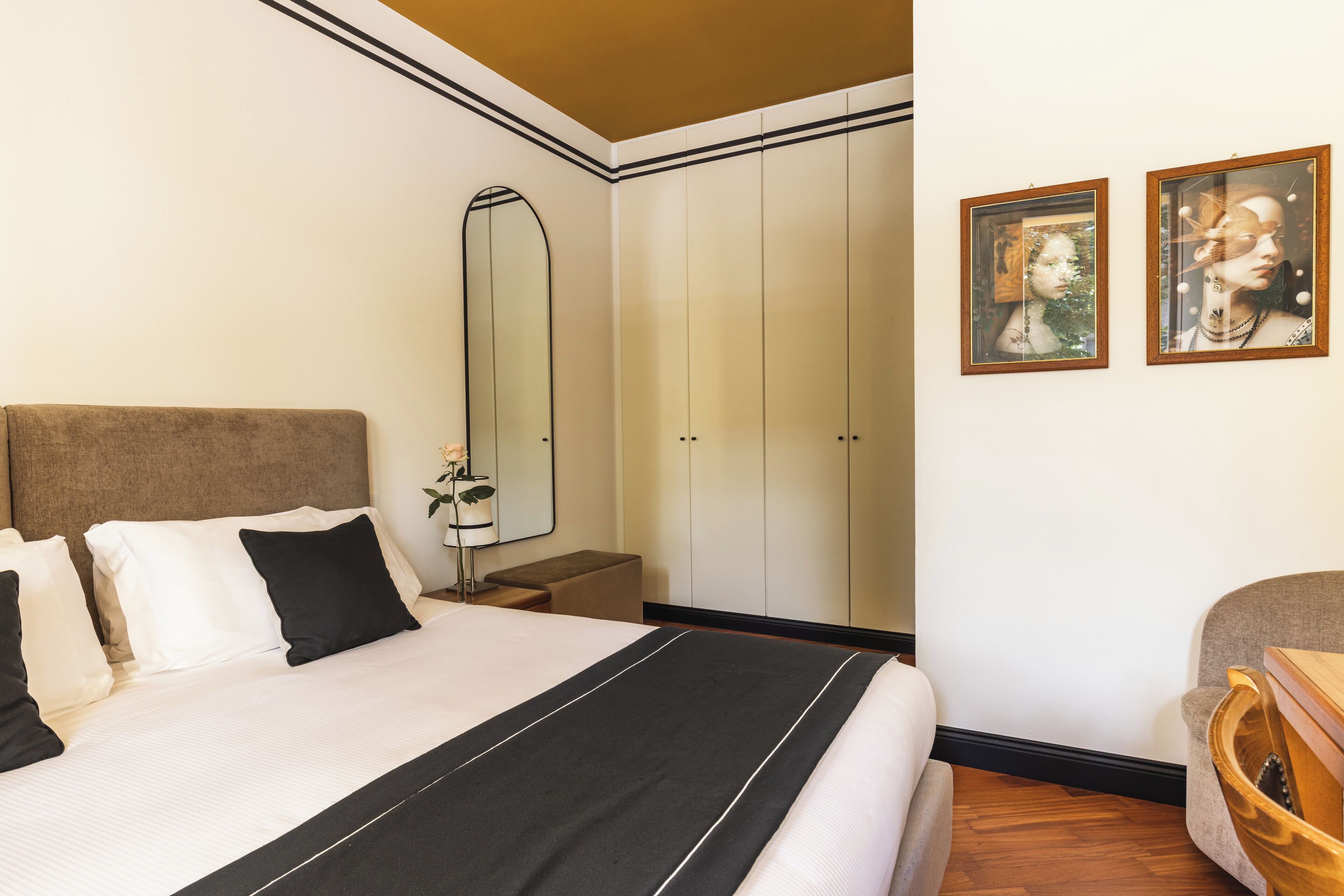 A hotel room with a large bed, a nightstand, a mirror, and two framed pictures on the wall.